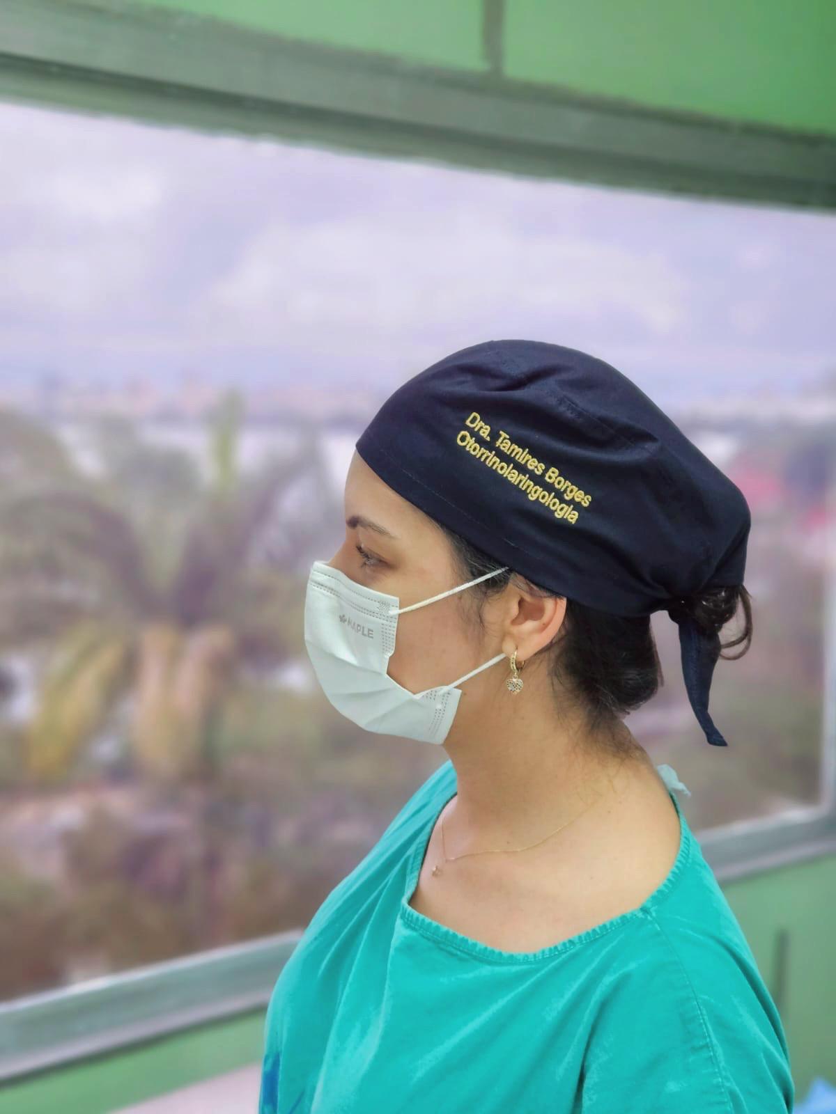 Dra. Tamires Borges, otorrinolaringologista, usando máscara e touca, com vista ao fundo.